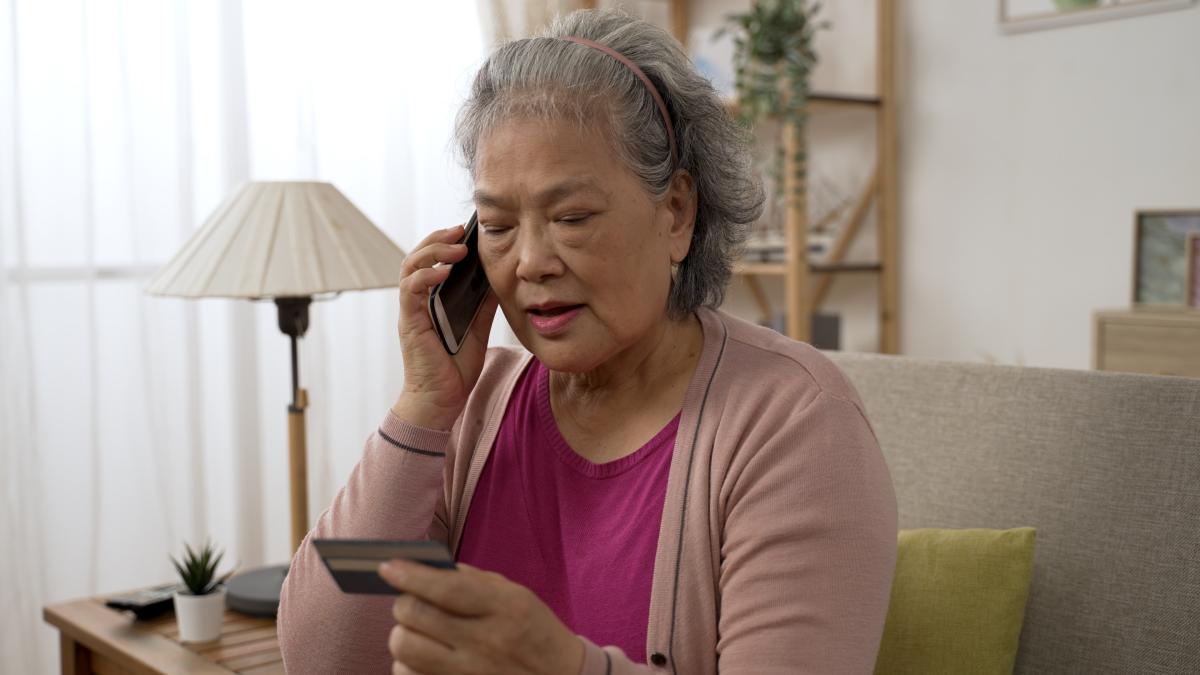 Older woman on the phone looking at a credit card with a pensive expression