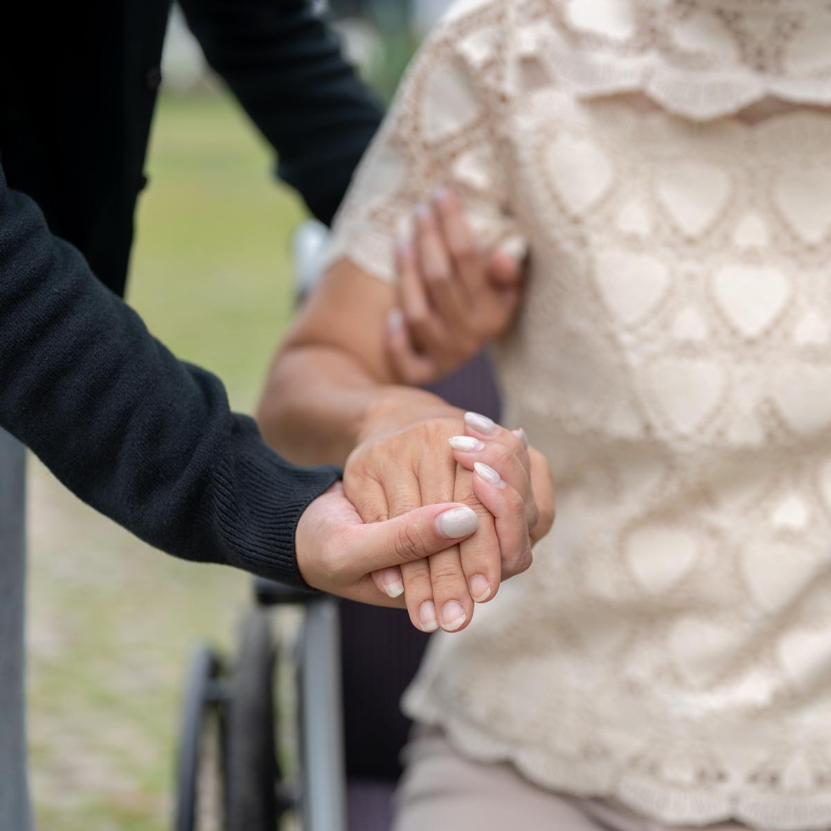 Younger Hand Providing Support to Arm of a Person in a Wheelchair Trying to Stand