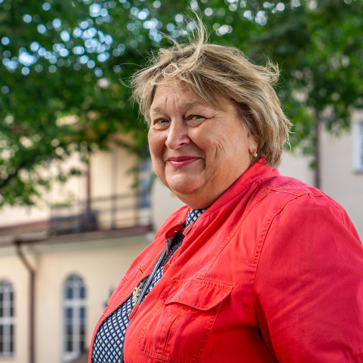 Older Woman Wearing Red Jacket Smiling at Camera While Outside