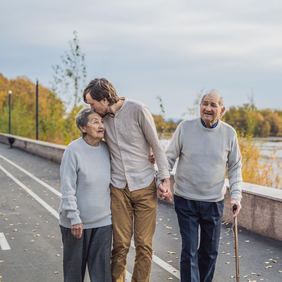 Adult Man Holds Hands with Senior Man while Hugging Senior Woman on Bridge