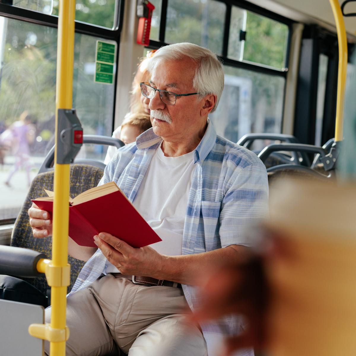 An older man sits on a bus reading a book
