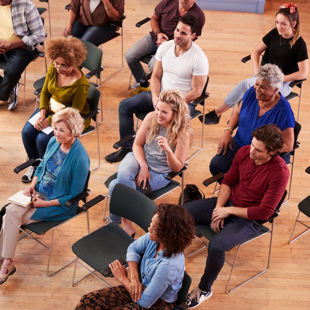 A group of people of all ages and varied races are seated and listening to a public forum