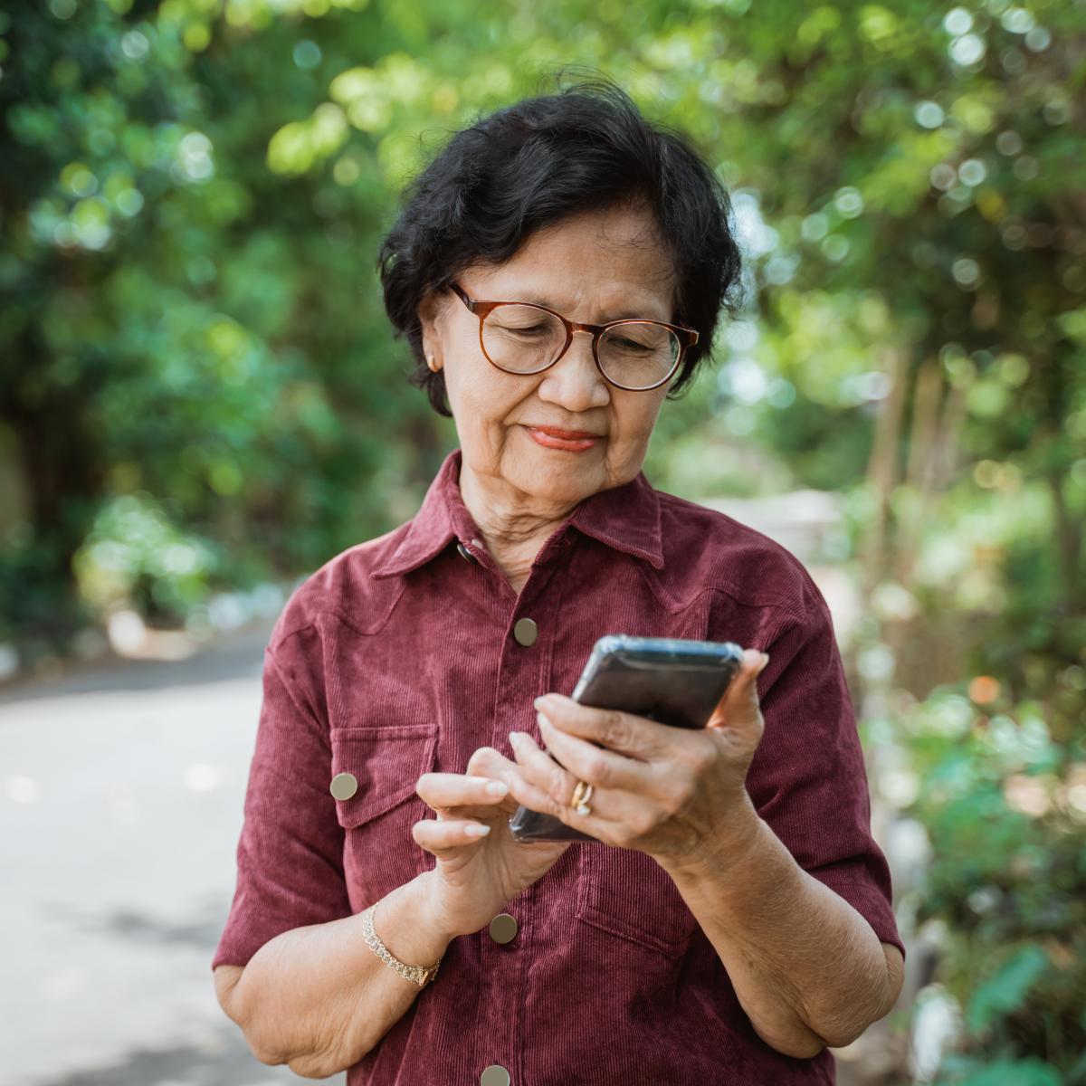 Older adult standing outside and looking at a mobile phone