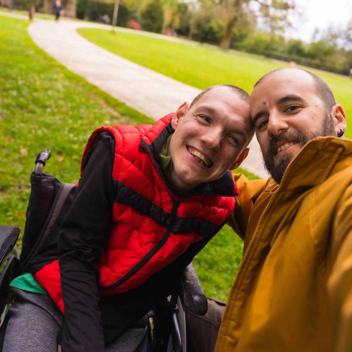 Older adult taking a selfie with a younger adult using a wheelchair