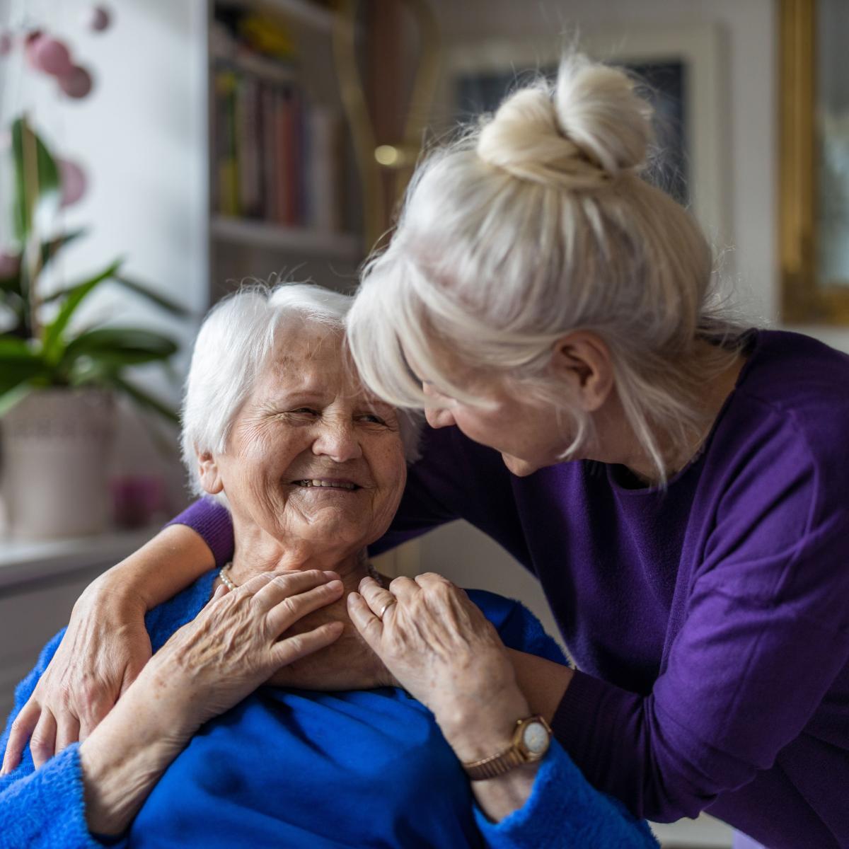Older adult woman receiving a hug while seated at a dining room table