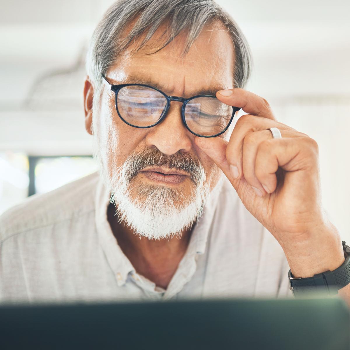 Older adult adjusting glasses while peering down at laptop screen