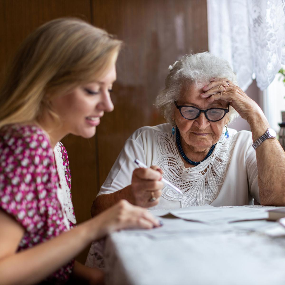 Older Adult Sitting at Kitchen Table with Younger Adult Looking at Papers