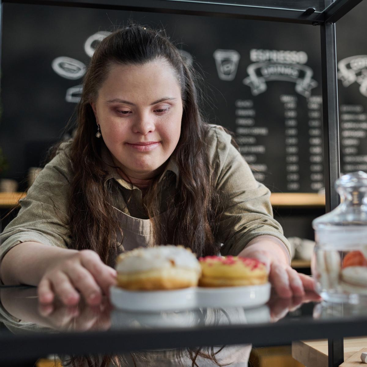 Young Adult Woman Living with Down Syndrome is Shown at Work in a Coffee Shop