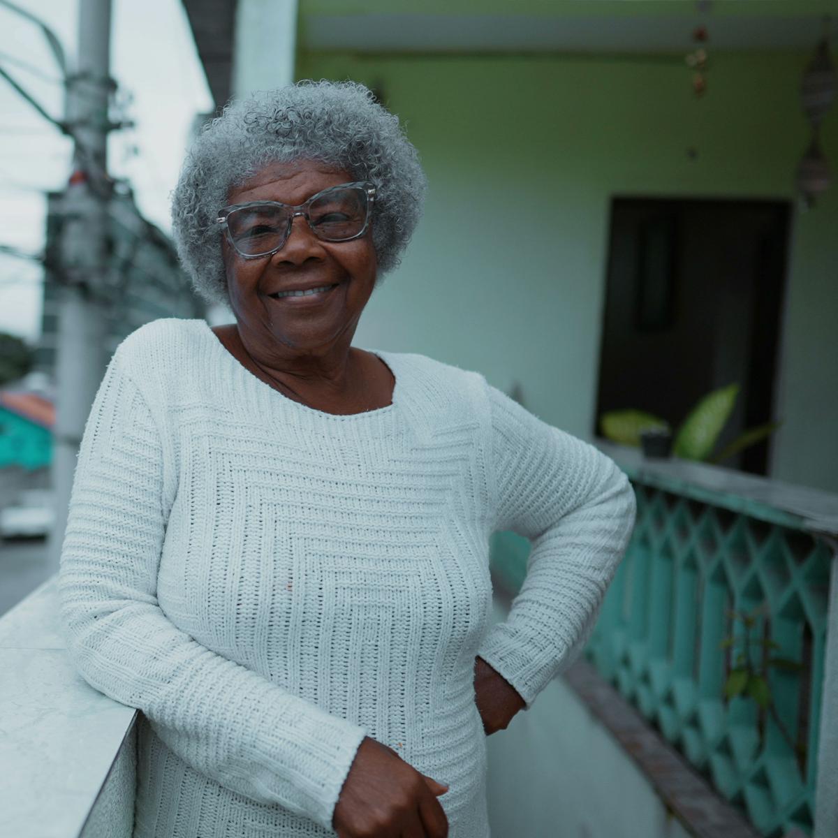 Older adult standing on outdoor balcony looking at camera with smile