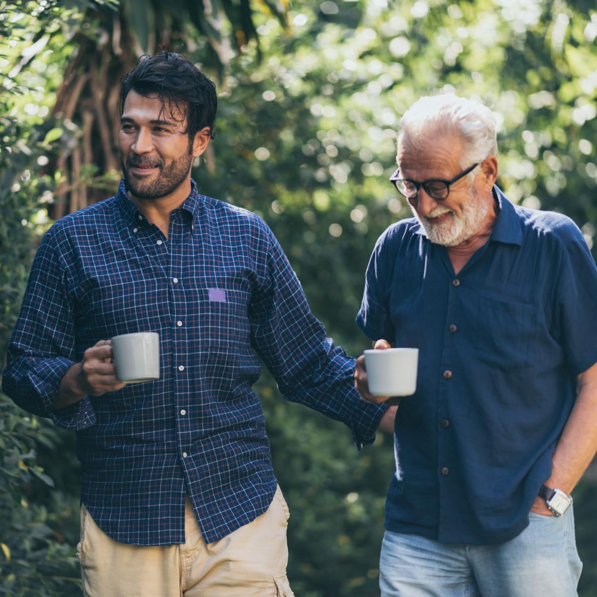 Older adult standing outside and holding a cup while talking to a younger adult